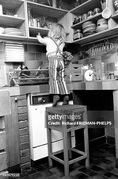 Les dangers de la maison, enfant en équilibre sur un tabouret attrapant de la vaisselle rangée sur une étagère.