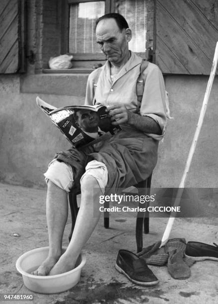 Homme âgé prenant un bain de pieds en lisant un magazine.