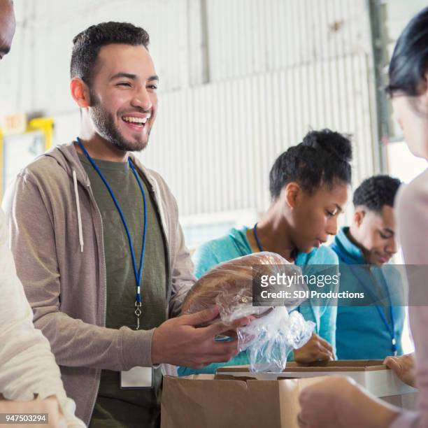 cheerful young male food bank volunteer passes out bread - natural disaster volunteer stock pictures, royalty-free photos & images
