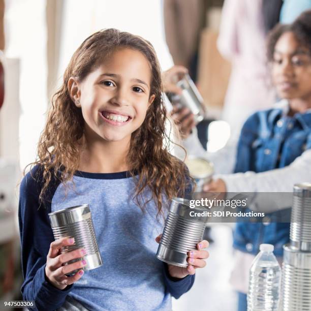 adorable little girl shows canned food to camera at food bank - emergency planning stock pictures, royalty-free photos & images