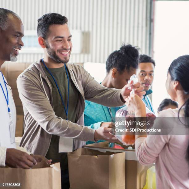 young male food bank volunteer passes out bags of fruit - civil defence stock pictures, royalty-free photos & images