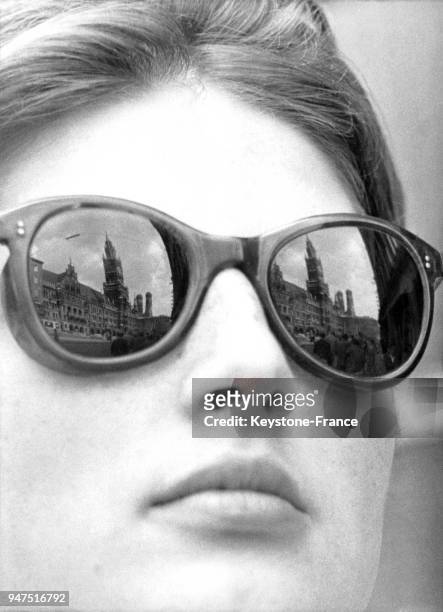 Jeune femme portant des lunettes noires, où se reflète les tours de l'hôtel de ville de Munich, Allemagne le 22 avril 1960.