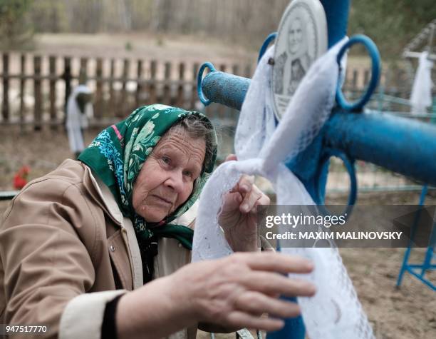 An eldery woman ties a ribbon around a cross at a cemetery in the village of Orevichi, inside the exclusion zone around the Chernobyl nuclear...