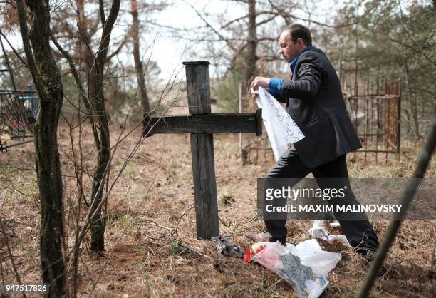 Man ties a ribbon around a cross at a cemetery in the village of Orevichi, inside the exclusion zone around the Chernobyl nuclear reactor, some 390...