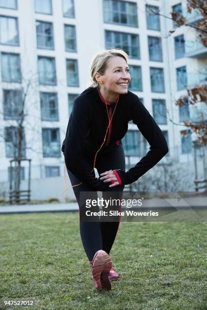portrait of a content mature woman stretching after a run in the city - winter sport stock-fotos und bilder