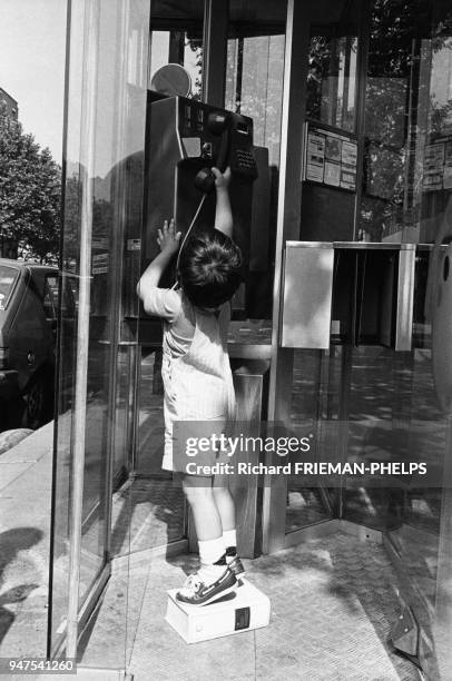 Enfant debout sur un dictionnaire pour atteindre le combiné d'une cabine téléphonique en France.