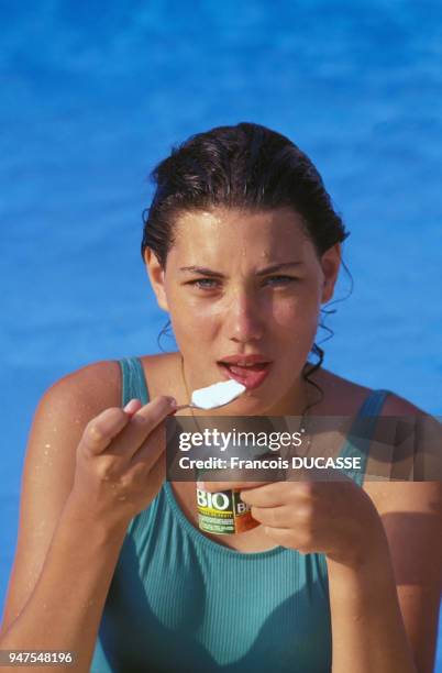 Jeune femme mangeant un yaourt ?Bio? sur une plage en France.