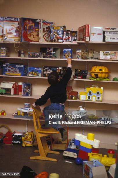 Enfant attrapant des jouets sur une étagère dans une ludothèque, en France.