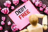 Conceptual hand text showing Debt Free. Concept meaning Credit Money Financial Sign Freedom From Loan Mortage written on Sticky Note Holding By Sculpture on the wooden background.