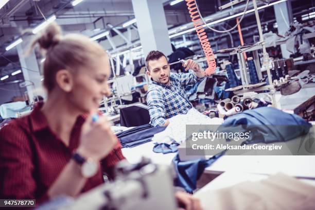 若い繊維労働者吹いて材料および彼の同僚からステッチ スレッドは彼を笑ってください。 - needlecraft ストックフォトと画像