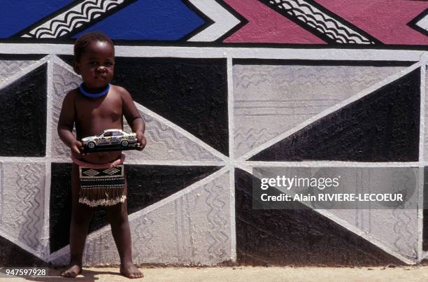 Enfant posant avec sa voiture peinte dans un village Ndébélé, en Afrique du Sud.