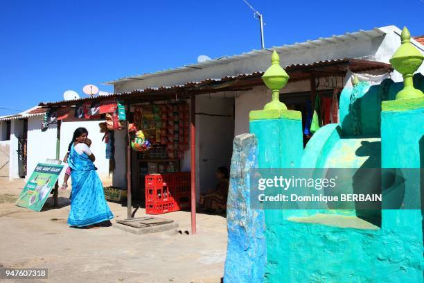 Une femme avec son enfant dans les bras devant une petite épicerie dans la rue principale du village indien de Bandipur, Inde du Sud.