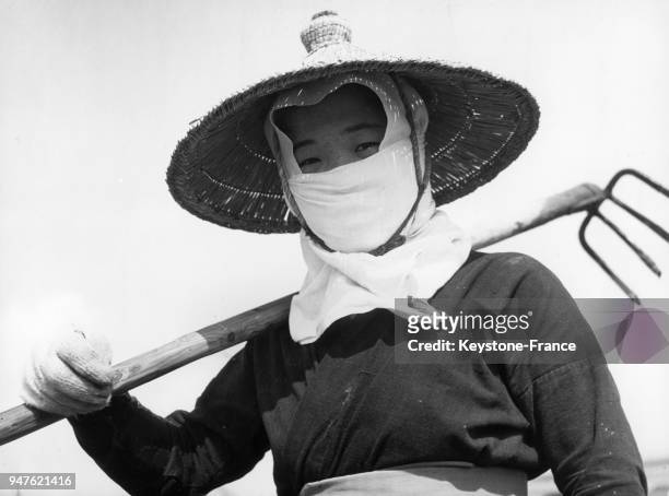 Portrait d'une paysanne portant un chapeau contre le soleil et le visage masqué pour se protéger des poussières, au Japon.