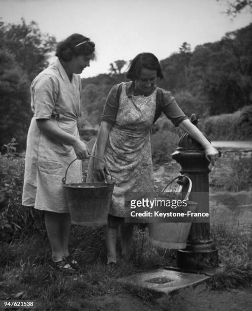 Deux femmes prennent de l'eau à la pompe à eau du village qui ne possède pas l'eau courante dans les maisons, circa 1950 au Royaume-Uni.