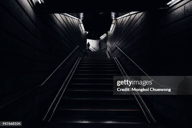 man walking into the light in the dark tunnel from underground - blak and white leaves fotografías e imágenes de stock