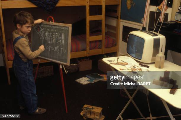 Enfant écrivant avec une craie sur un tableau tout en regardant la télévision.