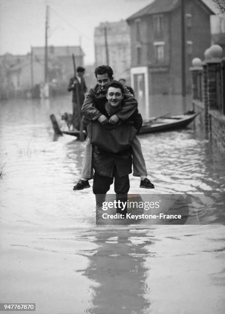 Un homme porte sur son dos un autre homme pour l'aider à traverser la rue inondée dans une ville de la banlieue parisienne, en France.