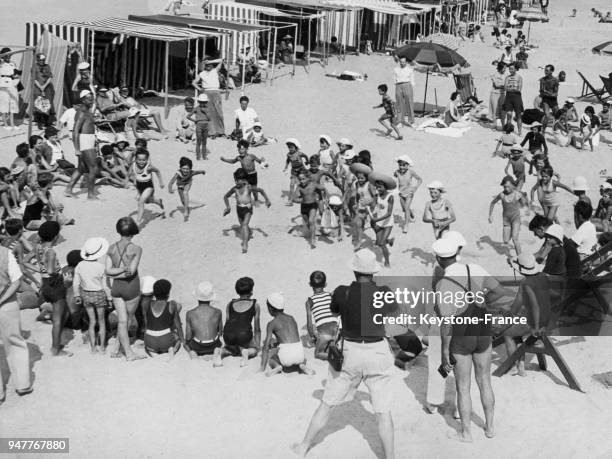 Des enfants se livrent à des jeux de plage en cercle sous la direction de leurs moniteurs en France.