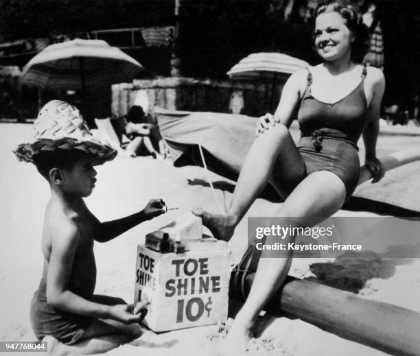 Ce petit garçon pose le vernis à ongle sur les orteils de cette jeune femme assise sur une plage.