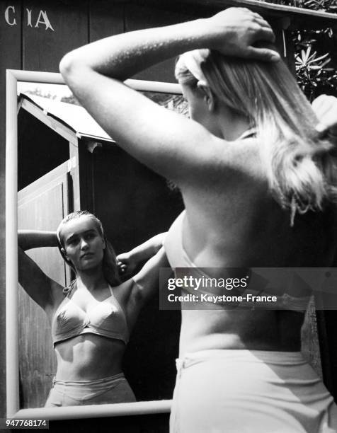 Une jeune femme blonde en maillot de bain se brosse les cheveux devant une glace.