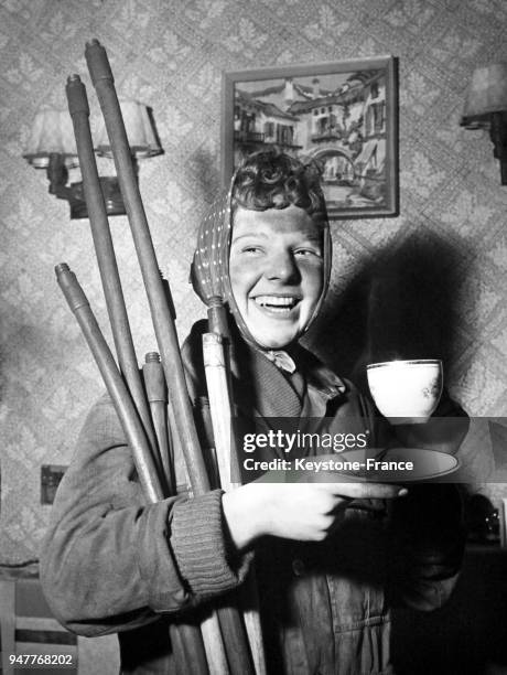 Une femme ramoneuse, couverte de suie et ses outils sous le bras, boit une tasse de thé dans un salon au Royaume-Uni.