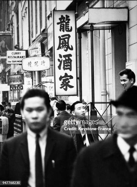Des hommes asiatiques en costume et chapeau dans une rue avec des enseignes en chinois.