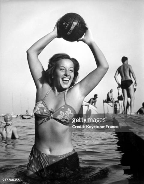 Une jeune femme en maillot de bain joue en riant avec un ballon dans l'eau.