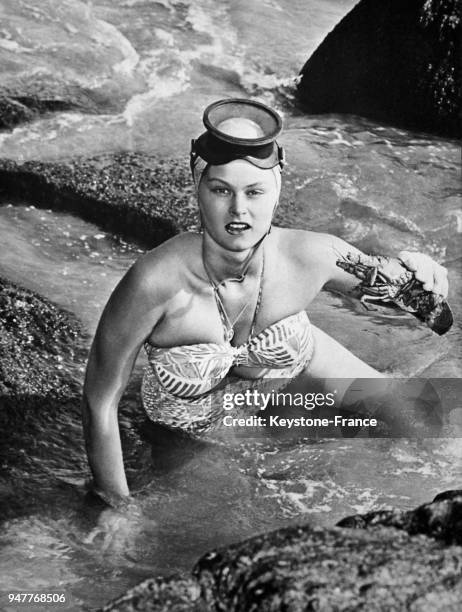 Une femme en maillot de bain et masque de plongée tient un homard qu'elle vient de pêcher à la main.