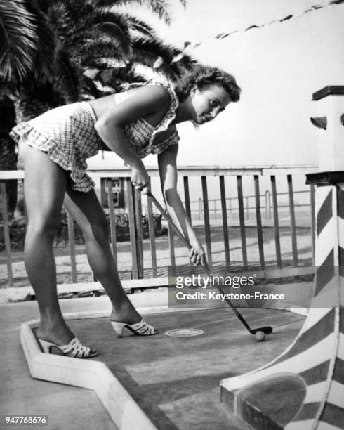 Une jeune femme en maillot de bain joue au mini-golf en bord de mer.