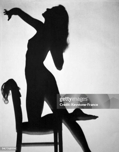 La silhouette d'une femme nue sur une chaise se découpe en ombre chinoise.