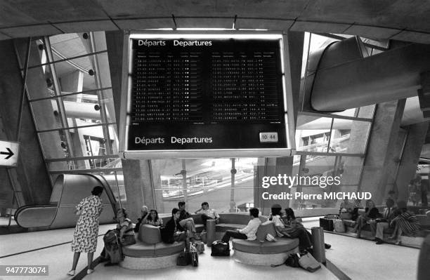 Les passagers dans une salle d'attente avec le tableau des départs à l'aéroport de Roissy, en France.