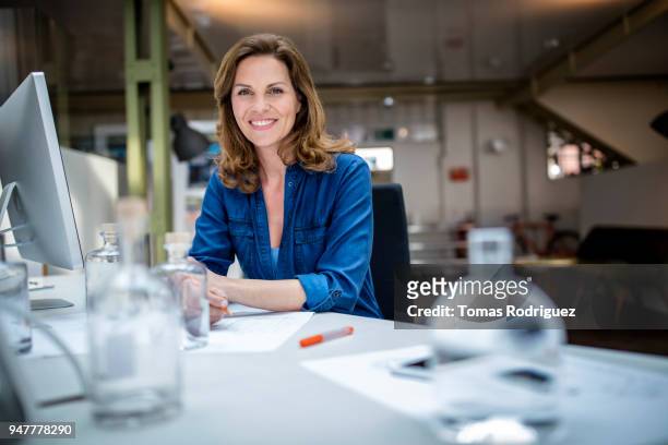 creative, smiling businesswoman on a desk with a computer - blusa azul imagens e fotografias de stock