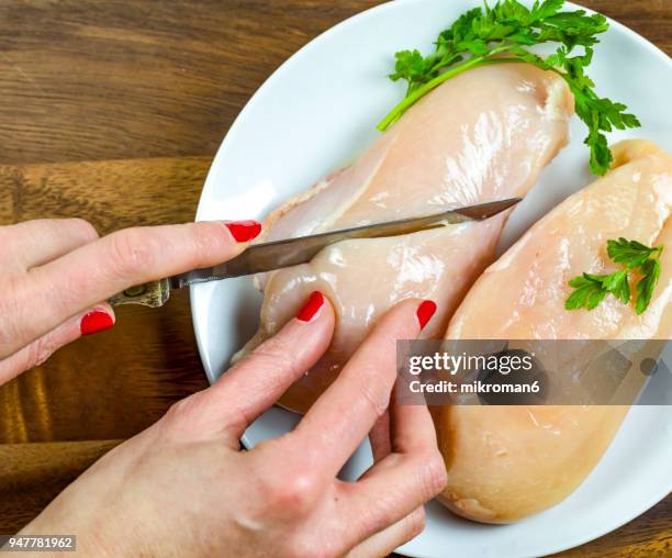 cropped hand of woman cutting raw chicken breast. - hoja de aluminio fotografías e imágenes de stock