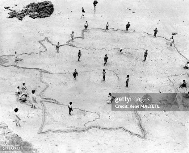 Enfants jouant au ballon sur un dessin de la France sur une plage, en France.