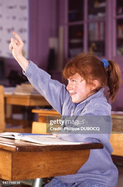 Petite fille levant le doigt en classe, dans une école primaire, France.