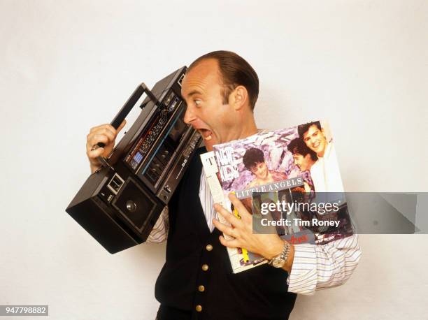 English drummer, singer-songwriter, record producer and actor Phil Collins of rock band Genesis, holding a portable radio and some records during a...