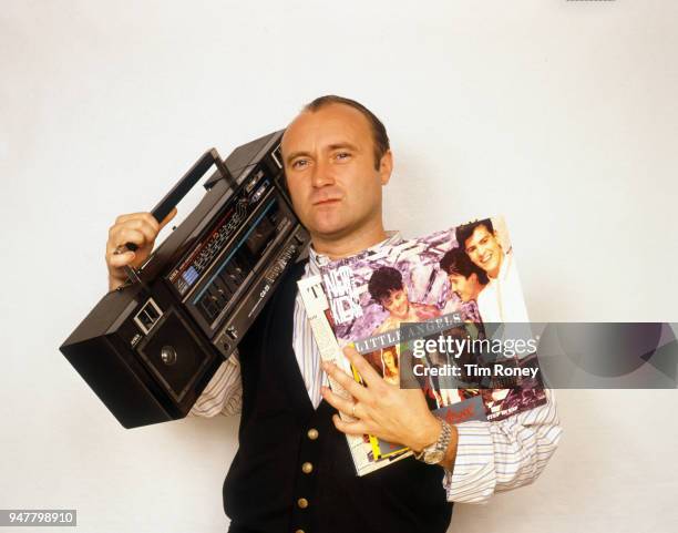 English drummer, singer-songwriter, record producer and actor Phil Collins of rock band Genesis, holding a portable radio and some records during a...