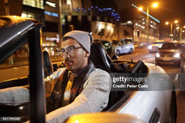 young man driving car through city at night - convertible top stock pictures, royalty-free photos & images