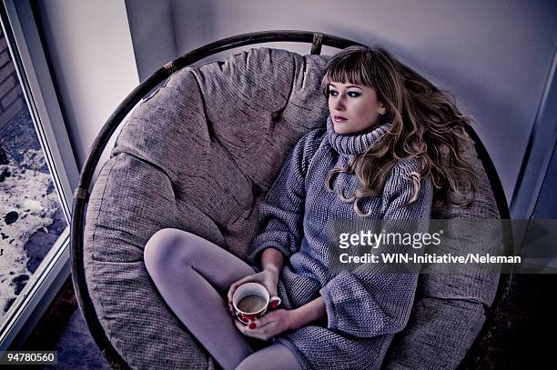 woman sitting in a ball chair and looking through  the window - egg chair stockfoto's en -beelden
