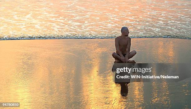 man sitting in lotus position on the beach at sunset, patnam beach, palolem, goa, india - palolem beach stock pictures, royalty-free photos & images