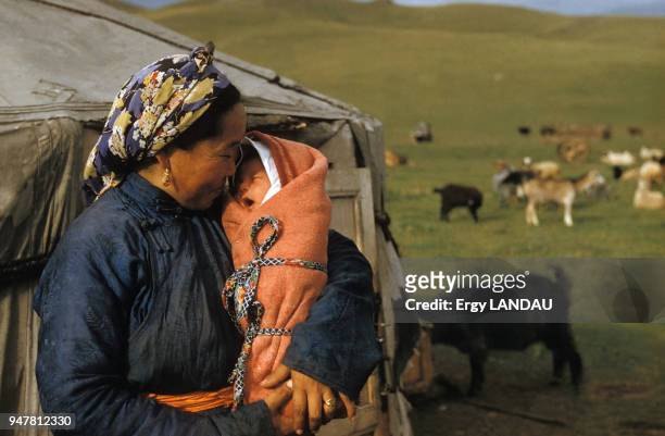 Femme tenant son bébé dans les bras devant sa yourte en Mongolie.