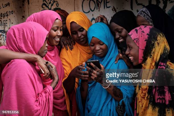 Young Somali refugee women look at a smartphone as they stand together at Dadaab refugee complex, in the north-east of Kenya, on April 16, 2018. The...