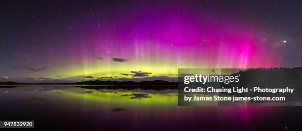 bright, colourful aurora display with reflections in water - southern lights foto e immagini stock