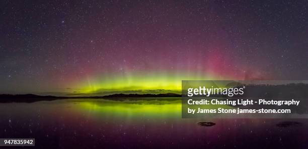 bright green display of the aurora australis or southern lights with reflection in water - aurora australis stock pictures, royalty-free photos & images
