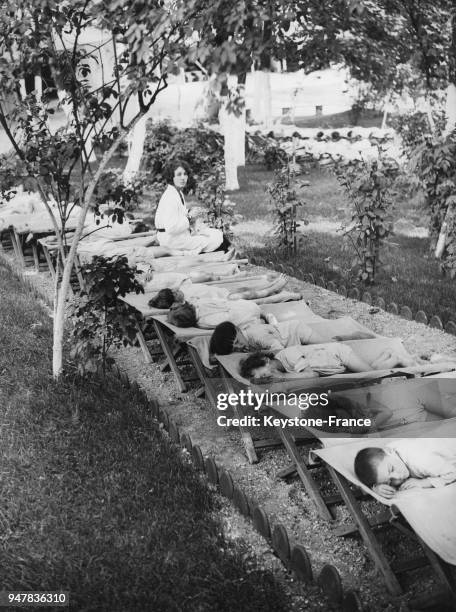 Une institutrice surveille des jeunes garçons endormis sur des lits pendant la sieste en plein air au Royaume-Uni.