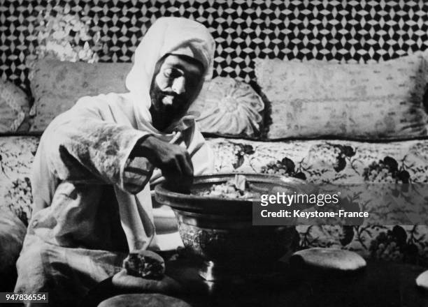 Un Marocain en tenue traditionnelle prend de la nourriture à la main dans un plat, à la manière orientale au Maroc.
