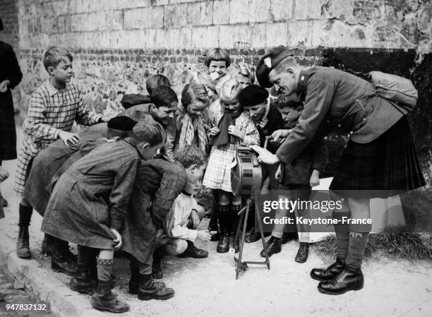 Groupe d'enfants regardant une sirène d'alarme que manipule un soldat Ecossais au quartier général, au Royaume-Uni.