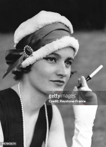 Une jeune femme avec un porte-cigarette à la main porte le chapeau 'Moulin Rouge' lors de la présentation de la collection de couture d'Elizabeth...