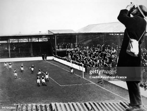 Un militaire surveille avec ses jumelles le ciel tandis qu'un match de football se déroule, au Royaume-Uni en 1940.