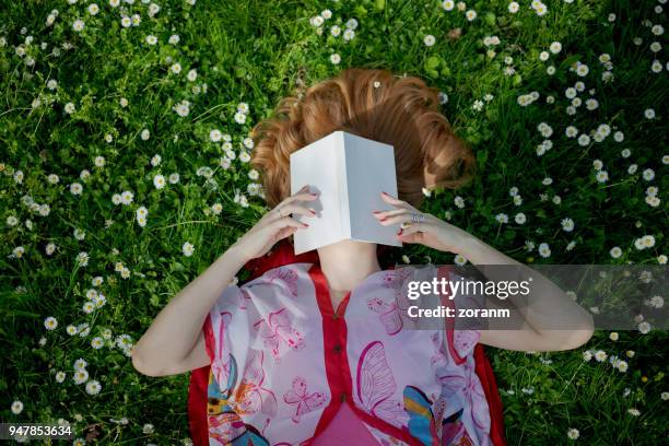 mujer tumbada sobre la hierba con su rostro oscurecido - mujer leyendo libro en el parque fotografías e imágenes de stock
